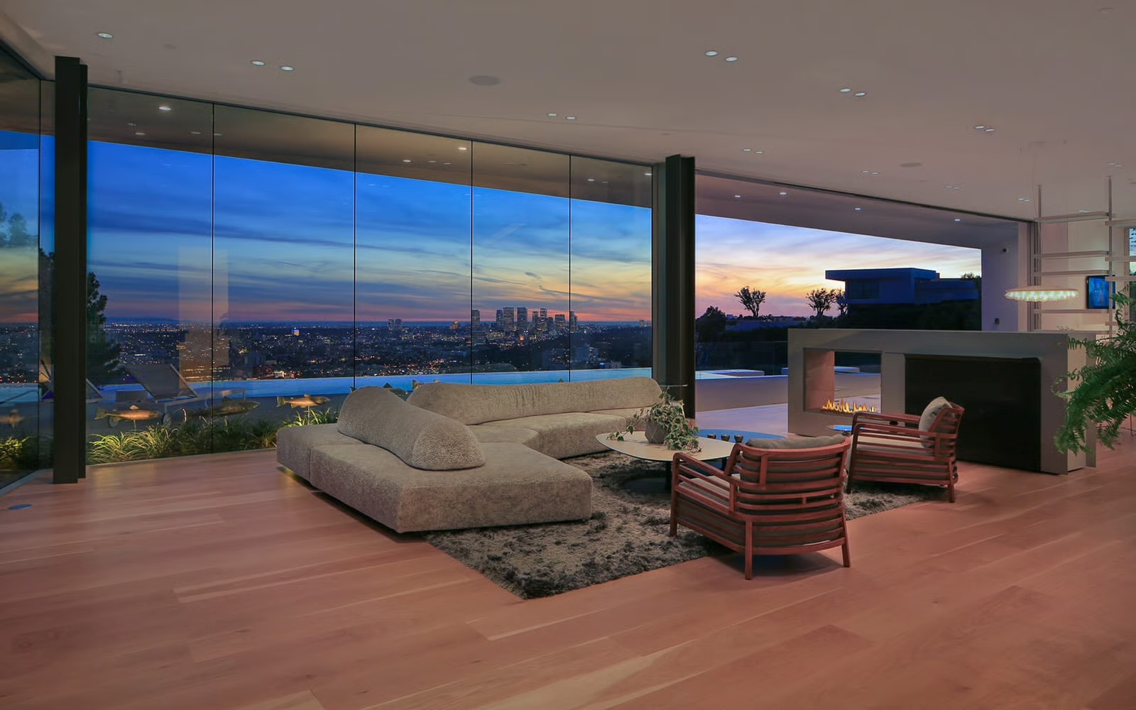 A glass-walled living room looking out over Los Angeles at dusk